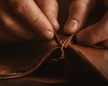 Hands stitching the edge of a brown leather piece